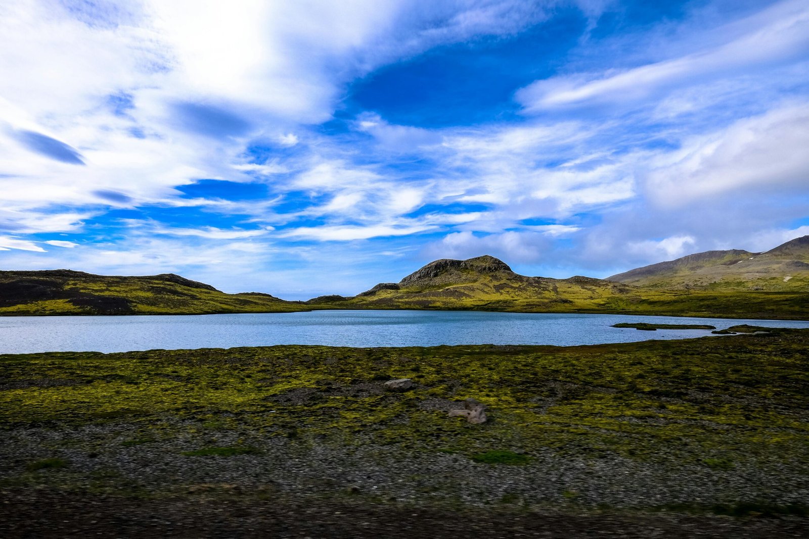 A tranquil mountain lake surrounded by lush green hills under a vibrant blue sky.